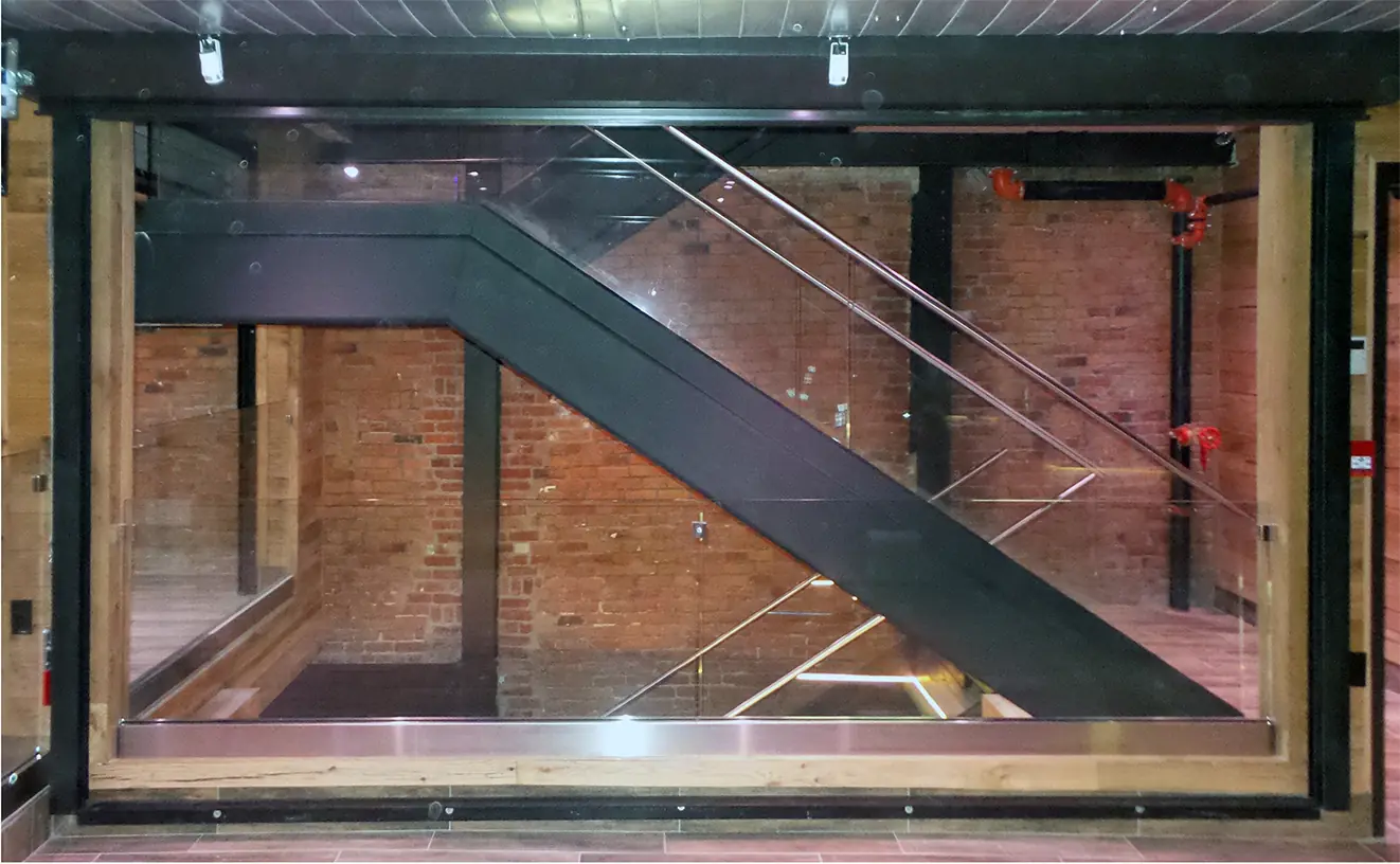 Escalier d’acier et de verre devant un mur de brique
